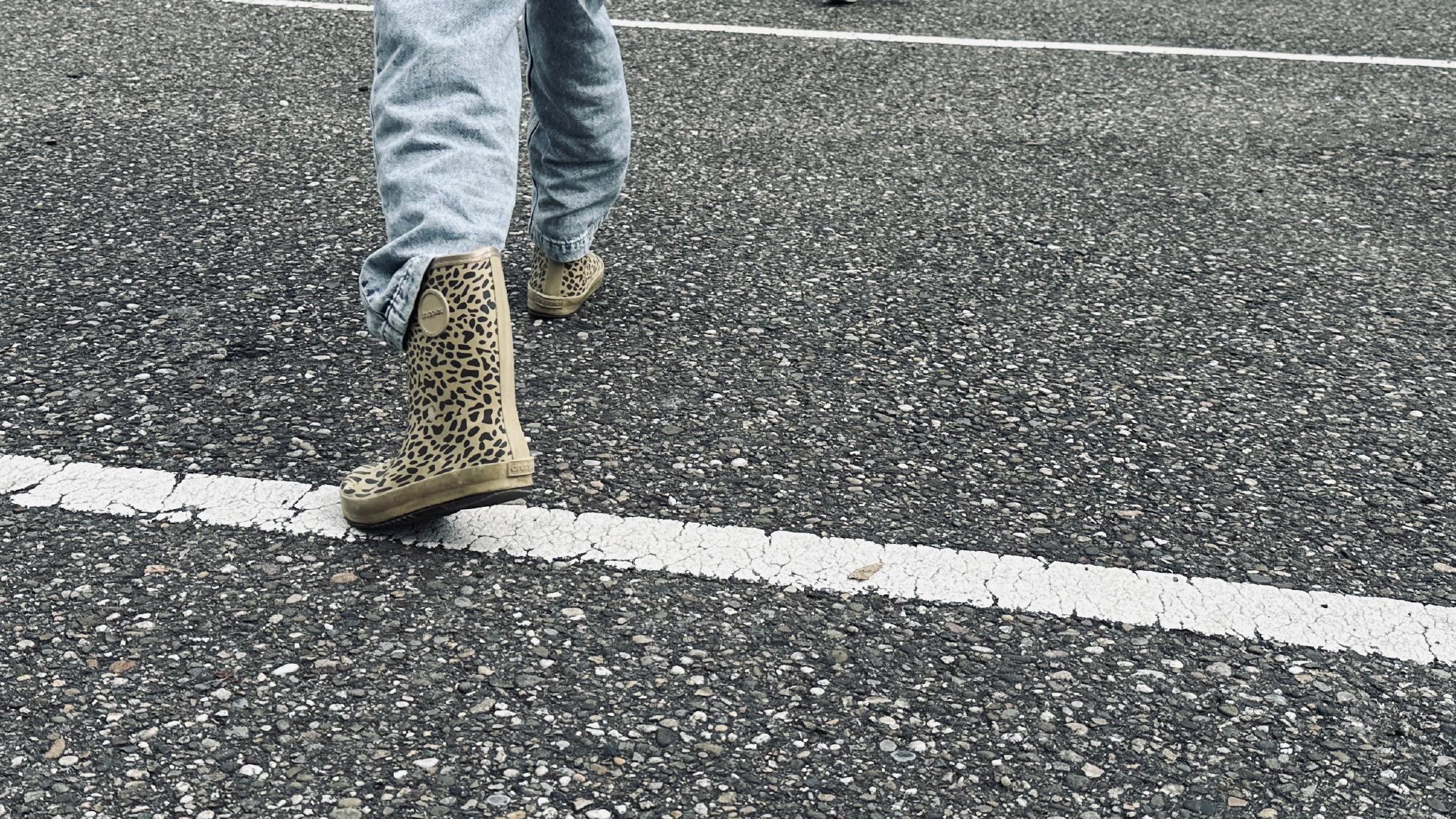 A girl stepping across a line on the ground. Only the boots and part of her jeans can be seen.